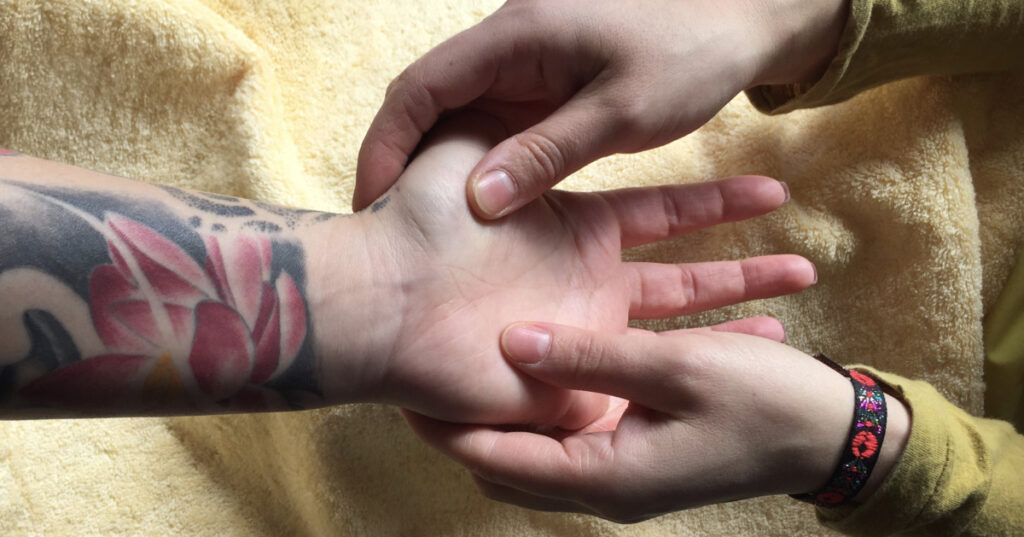 Achtsame Handmassage an einer tätowierten Hand als Symbol für das direkte Spüren und das Aktivieren vom Körpergefühl bei Entscheidungen.