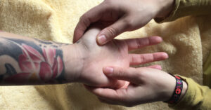 Achtsame Handmassage an einer tätowierten Hand als Symbol für das direkte Spüren und das Aktivieren vom Körpergefühl bei Entscheidungen.